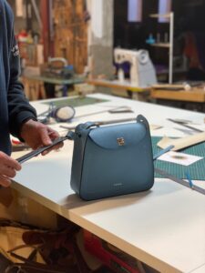 Dans un atelier de fabrication de sacs en cuir, un artisan travaille sur un sac bleu
