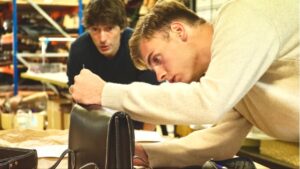 Deux artisans s'affairent à la réalisation d'un sac en cuir dans un atelier français