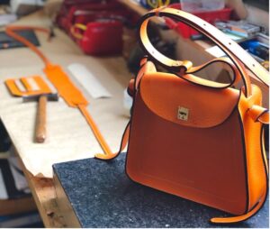 Un sac en cuir orange trônant sur une table au sein d'un atelier d'assemblage français
